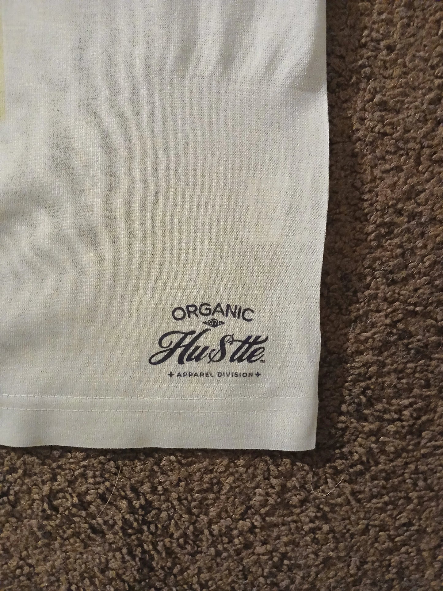 Close-up of a white fabric with 'Organic Hustle' logo on a brown textured surface