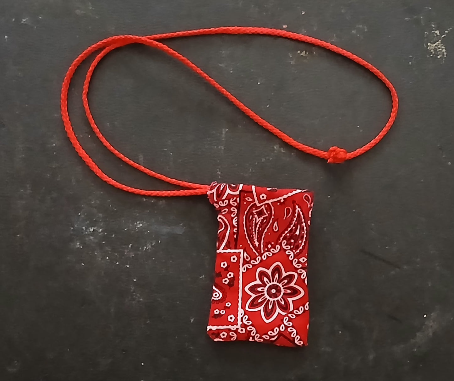 Red bandana-patterned pouch on a red string against a dark background