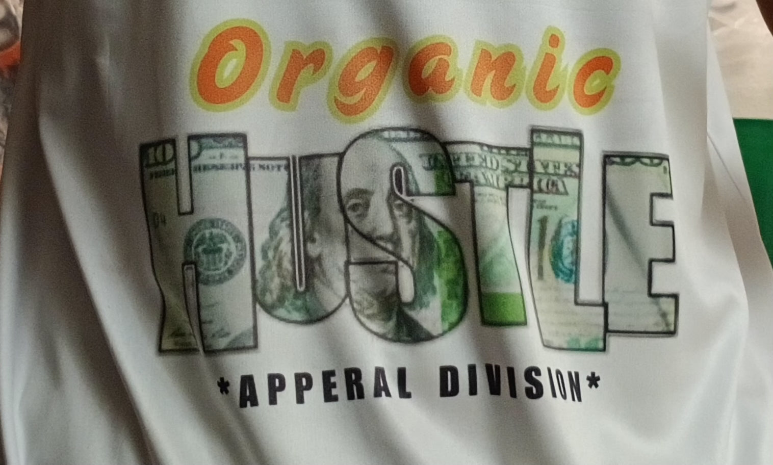 T-shirt with 'Organic Hustle' design featuring dollar bills and text on a white background