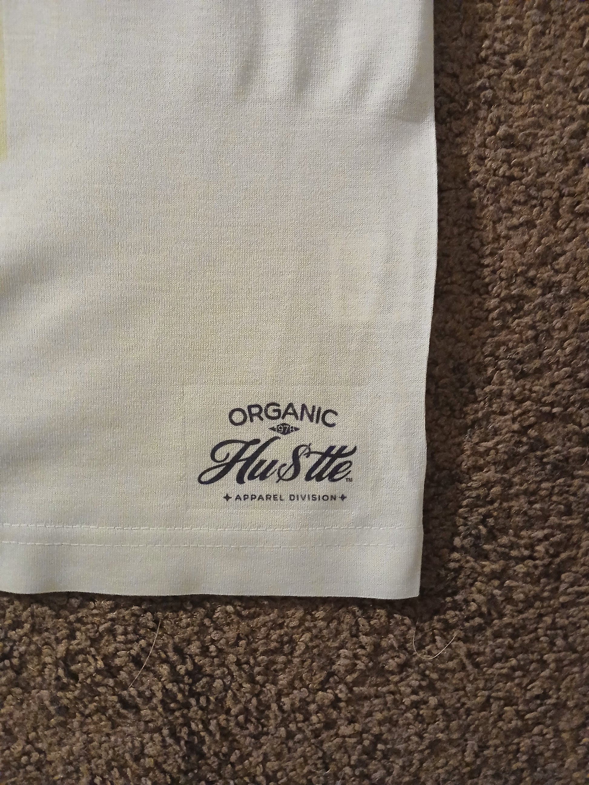 Close-up of a white fabric with 'Organic Hustle' logo on a brown textured surface