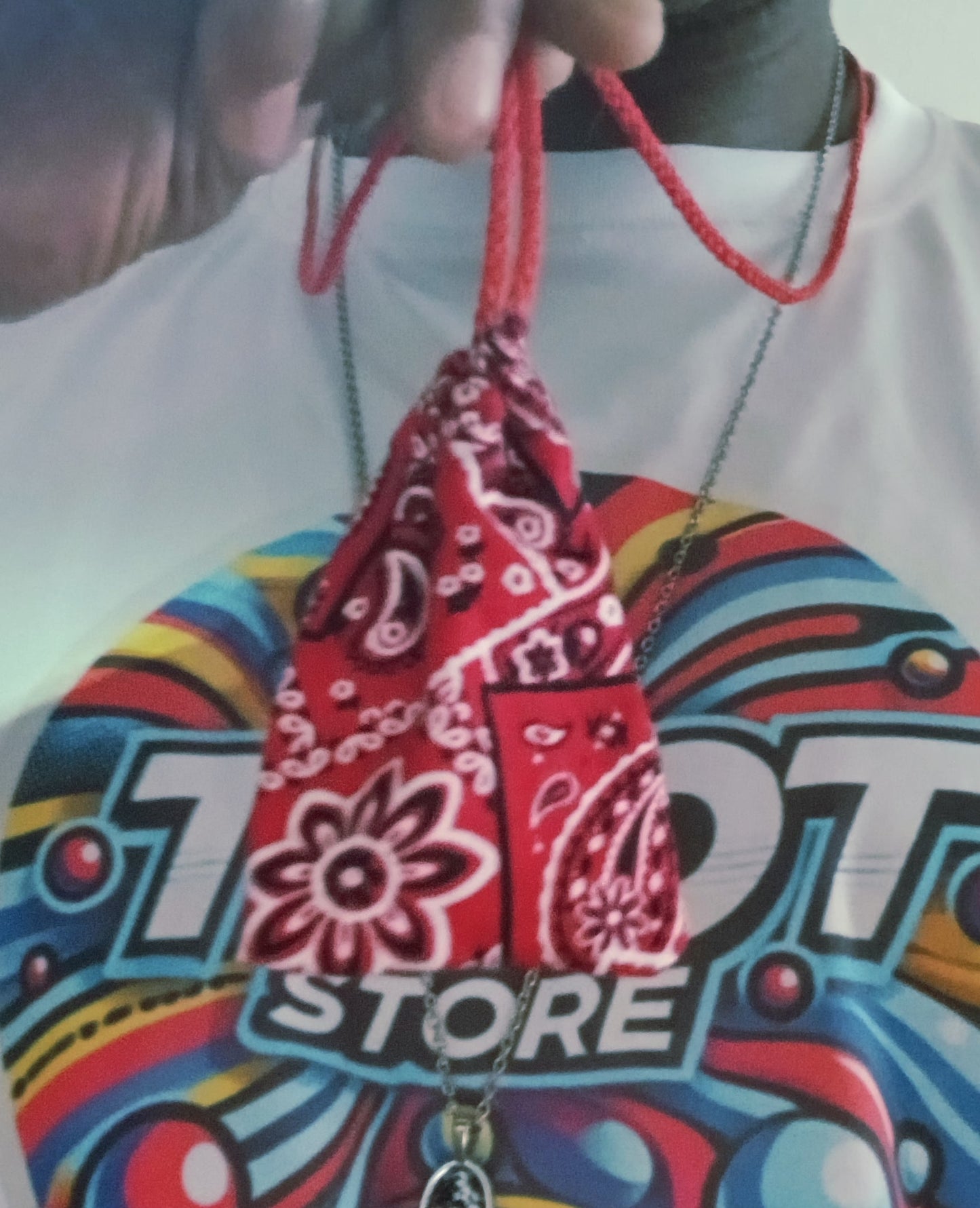Red bandana pouch held by a hand with a colorful 'Motor Store' shirt in the background