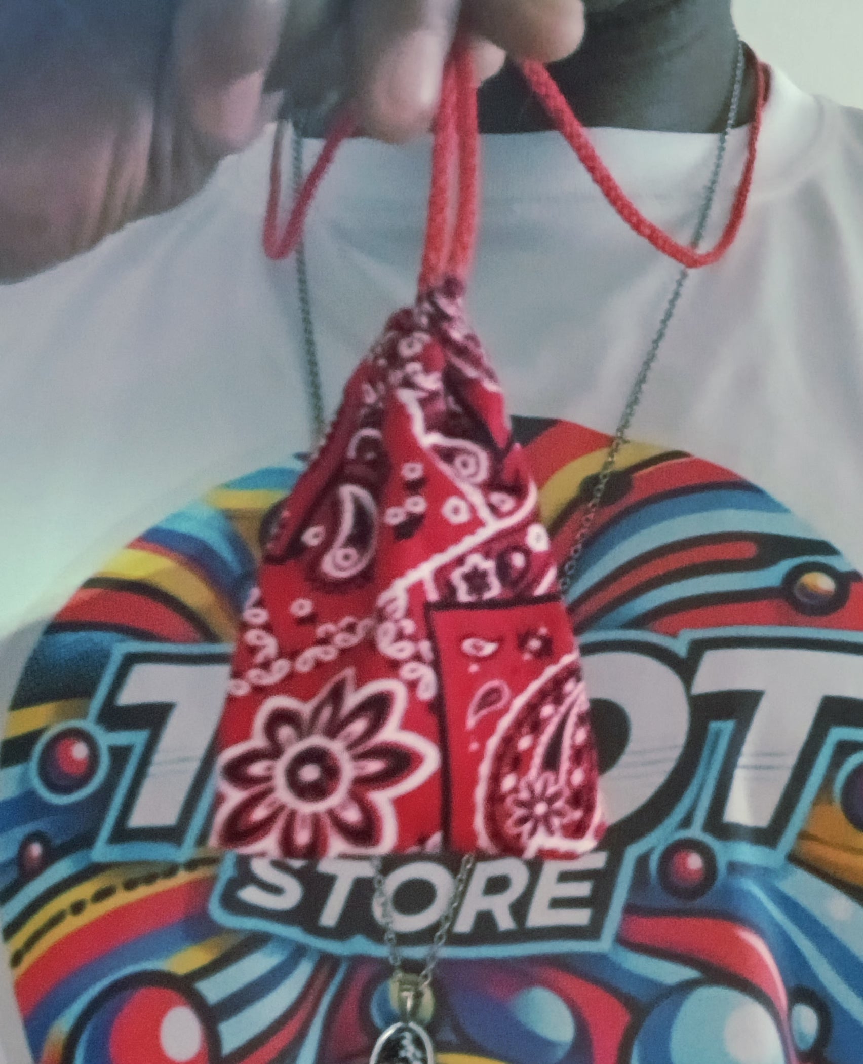Red bandana pouch held by a hand with a colorful 'Motor Store' shirt in the background