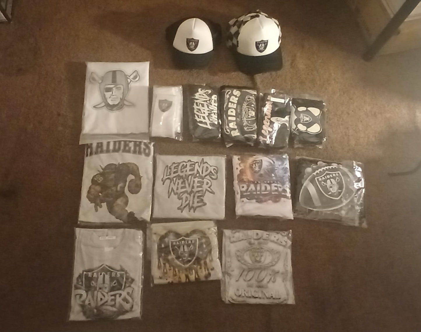 Collection of Oakland Raiders merchandise including t-shirts and hats on a carpeted floor.