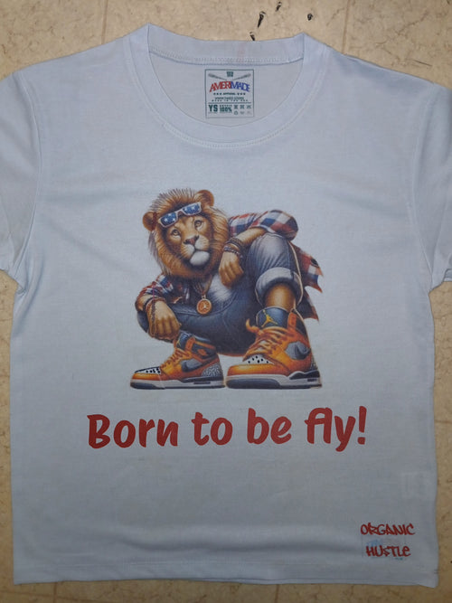 White t-shirt with a graphic of a lion wearing sneakers and a hat, with 'Born to be fly!' text, on a wooden surface.