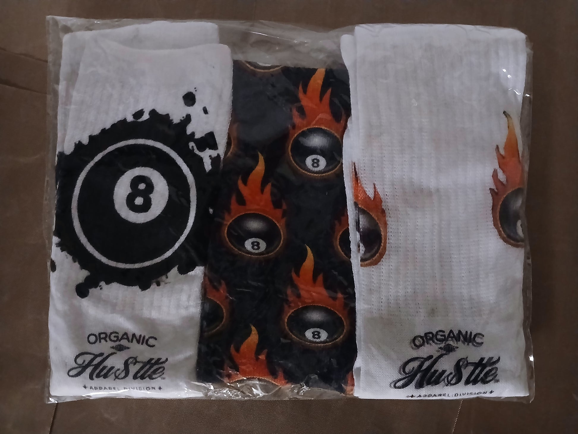 Three pairs of socks with '8 Ball' design and 'Organic Hustle' branding on a brown surface.