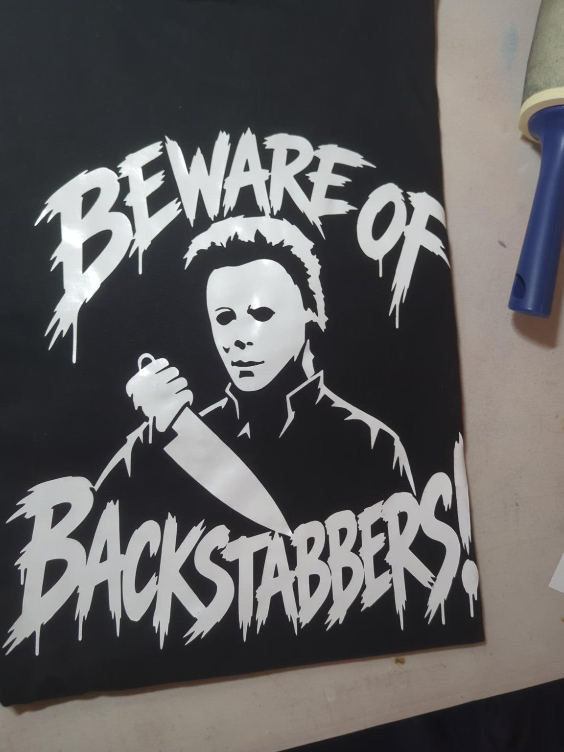 Close-up of actual white Beware of Backstabbers artwork on black fabric; sleeve length not visible