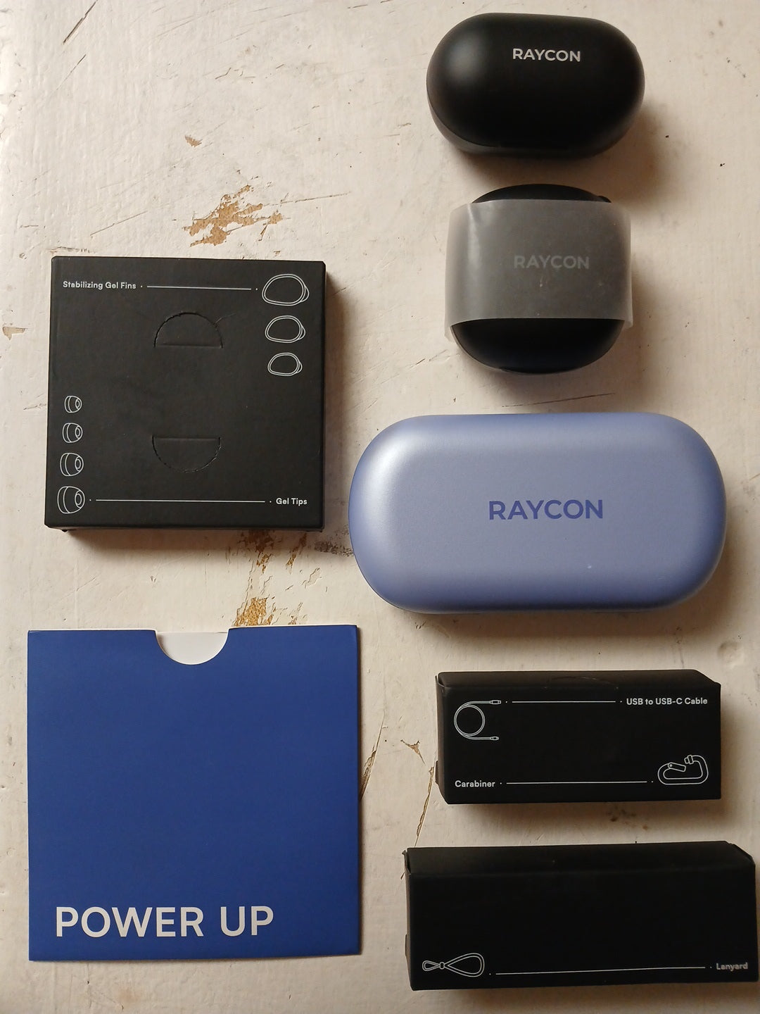 Collection of Raycon electronic devices and accessories on a textured surface